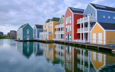 Houten, The Netherlands - April 25 2023. Row of colourful wooden lakeside houses. Reflected in the water of lake De Rietplas. Diminishing perspective.
