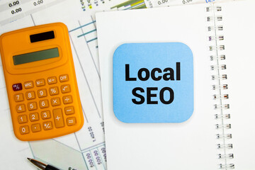 A laptop, glasses, a pen, a calculator, a cup of coffee, the text LOCAL SEO lie on a table with...