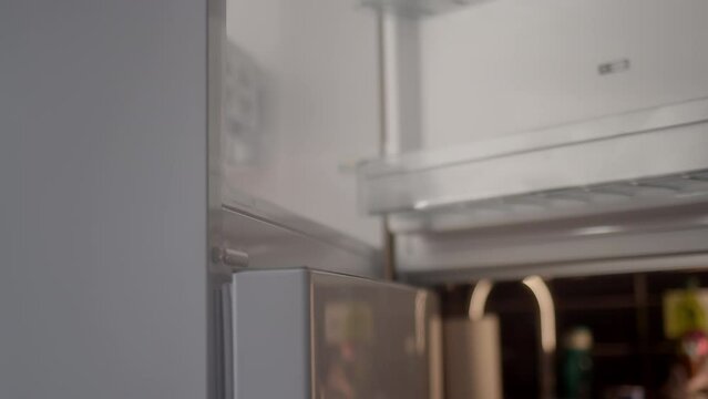 Close-up view, unrecognizable man with tattoos on his arms opens fridge freezer. concept of freezing food in refrigerator in kitchen.