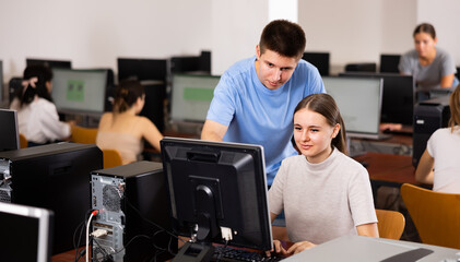 Positive male student explaining the topic to female friend while she is studying computer science on the pc in the classroom