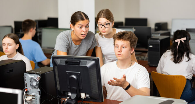 Two clever female students helping to male classmate while he is learning computer science in the computer room. High quality photo