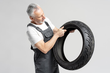 Fototapeta na wymiar Smiling senior man 60s, mechanic technician, salesman in repair shop, showing new motorcycle tire