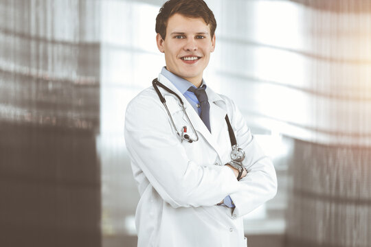 Positive young doctor is smiling at camera. Portrait of professional physician in sunny clinic