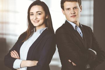 Friendly young colleagues are standing as a team with crossed arms in sunny office. Successful business people at work