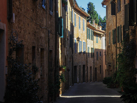 Fototapeta Narrow street in the historic center of one of the cities of Tuscany, Italy, the walls of San Quirico d'Orcia, Italian village a UNESCO World Heritage Site, a medieval town, a play of shadow and light
