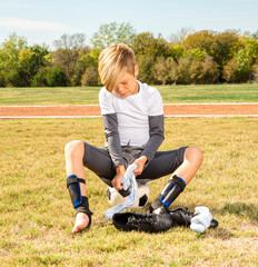 Young boy soccer player getting dressed for a game while sitting on a soccer ball