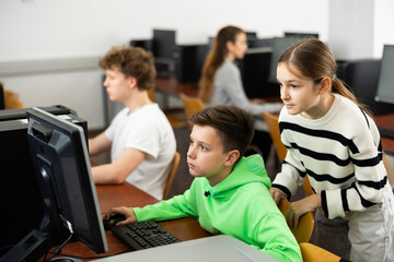 Fototapeta premium Positive female teacher helping focused preteen schoolboy studying in college library computer lab..
