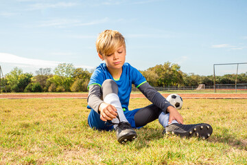 Male youth soccer player sitting on the field looking bored or uninterested in the game