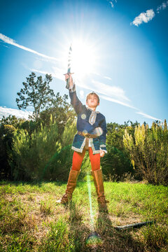 Young boy in prince costume raising his sword into the air in a triumphant pose