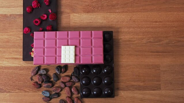 Ruby dark and white chocolate bars on a wooden table with cocoa seeds. Top view. High quality 4k footage