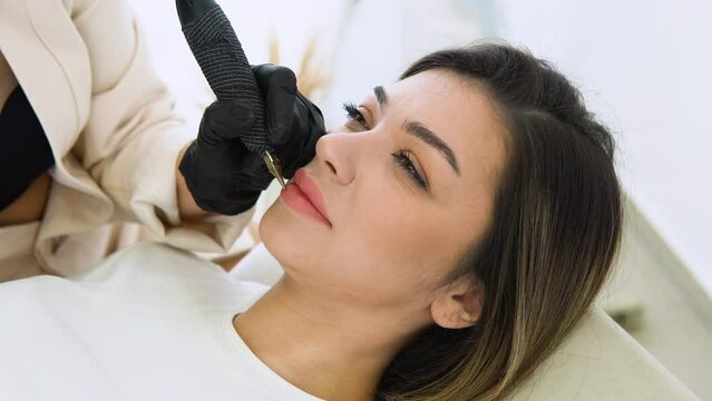 Process woman applying permanent tattoo makeup on lips in beautician salon