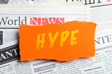 Orange paper piece with word Hype on pile of newspapers, top view
