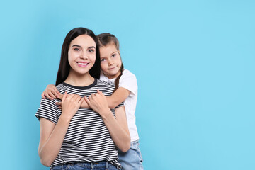 Happy woman with her cute daughter on light blue background, space for text. Mother's day celebration