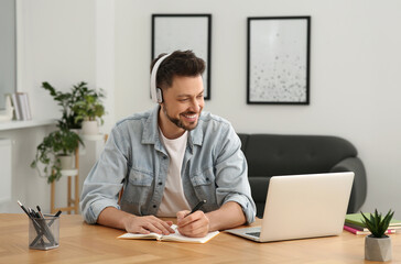 Fototapeta premium Man in headphones studying on laptop at home. Online translation course