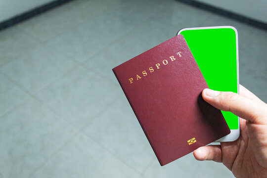 Point of view of a man holding his passport and his cell phone with the green screen in an airport hall
