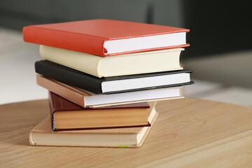 Stack of different hardcover books on wooden table indoors