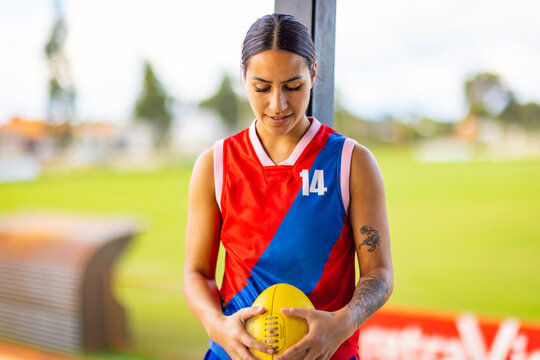 dark-haired young woman wearing team uniform and looking down at the football in her hands