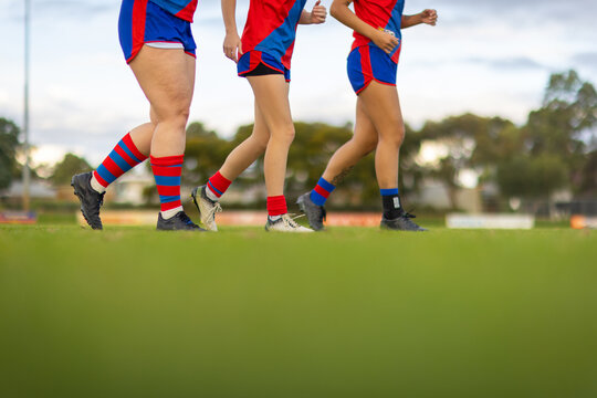 the legs of three female football players jogging onto a football oval