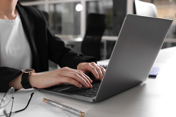 Woman working with laptop at white desk in office, closeup