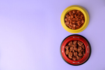 Wet pet food in feeding bowls on violet background, flat lay. Space for text