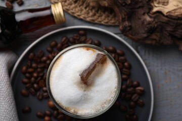 Glass of coffee, bottle with delicious syrup and beans on light grey table, closeup
