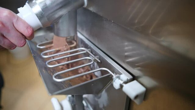 Hands of a pastry chef pouring chocolate ice cream formula from pasteurizer to freezer. High quality 4k footage