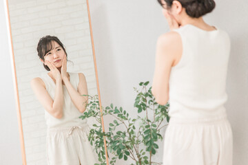 顔のたるみ・ほうれい線に悩む鏡を見るアジア人女性
