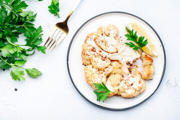 Baked cauliflower steak with garlic butter and spice on plate, white table background, top view