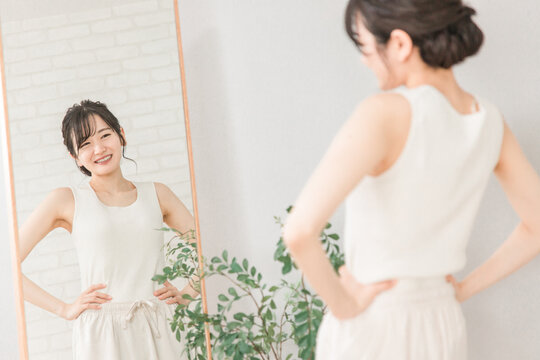 鏡で自分の体型・スタイルをチェックする笑顔のアジア人女性
