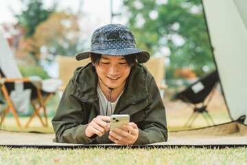 秋冬のキャンプ・アウトドアでスマホを使う若いアジア人男性キャンパー
