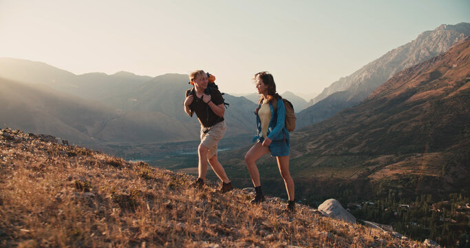 Caucasian couple hiking together with backpacks, helping each other on their way up the mountains - freedom, active lifestyle concept 