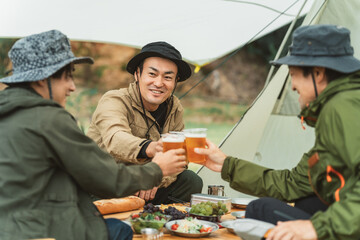 男友達とキャンプ場でビールを持って乾杯するアジア人キャンパー
