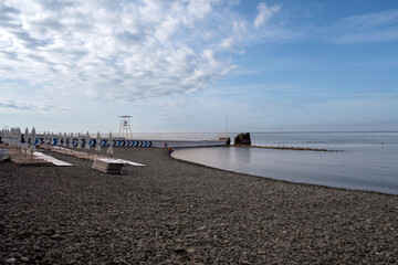 A deserted beach on the coast of Sochi with sun beds and umbrellas against the background of the calm Black Sea, Adler, Krasnodar Territory, Russia