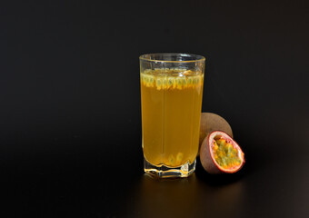 A glass of freshly squeezed fruit juice with seeds and slices of ripe passion fruit on a black background.