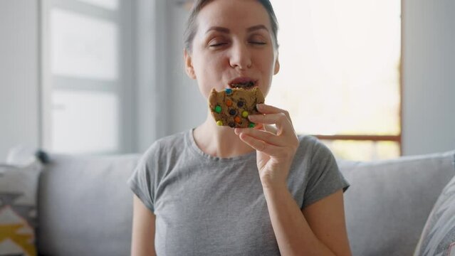 Hungry woman biting and chewing colourful chip cookie close-up
