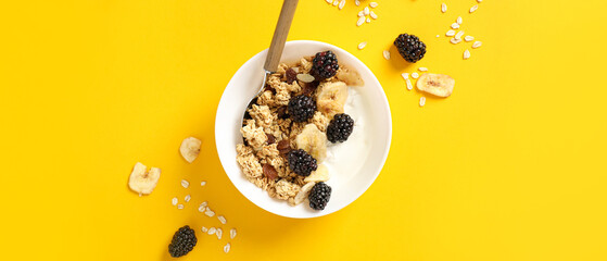 Tasty granola with yogurt in bowl on yellow background