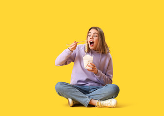 Young woman eating Chinese noodles on yellow background