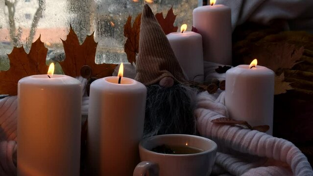Thanksgiving and Hello Fall Halloween concept Celebrating autumn holidays at cozy home on the windowsill Hygge aesthetic atmosphere Autumn leaves gnome, spices and candle on knitted white sweater in