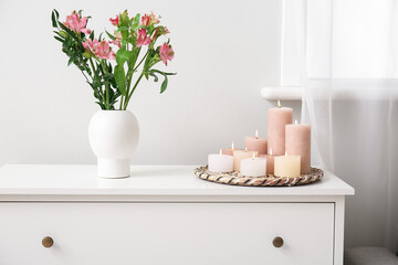 Burning candles and vase with beautiful alstroemeria flowers on chest of drawers