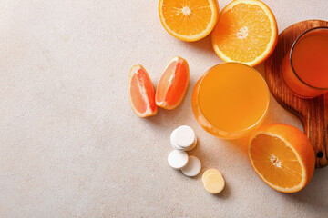 Glasses of vitamin C effervescent tablet dissolved in water and fruits on grey grunge table