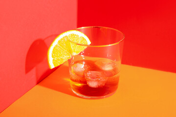 Glass of rum with ice cubes and orange slice on red background