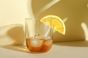 Glass of rum with ice cubes and orange slice on beige background