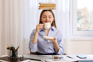 Young businesswoman with books drinking coffee in office. Balance concept