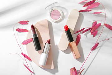 Composition with beautiful lipsticks, eyeshadows, plaster podiums and dried flowers on light...