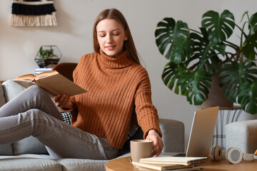 Fototapeta premium Female student with cup of tea reading book at home