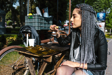 young latin woman with braids hair eating mexican tamales street food on park in Mexico city, hispanic people	