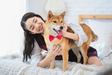 Beautiful asian woman playing with her dog with fun expression on the bed in bedroom.