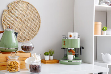 Modern coffee machine, cups, snacks and jar with coffee beans on table near white wall