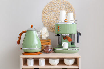 Modern coffee machine, electric kettle, cups and jar with cookies on table near white wall