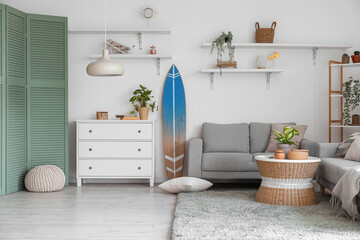 Interior of light living room with surfboard, commode and sofas